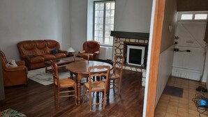 Een woonkamer met een open haard, een leren bank, houten stoelen en een eettafel.