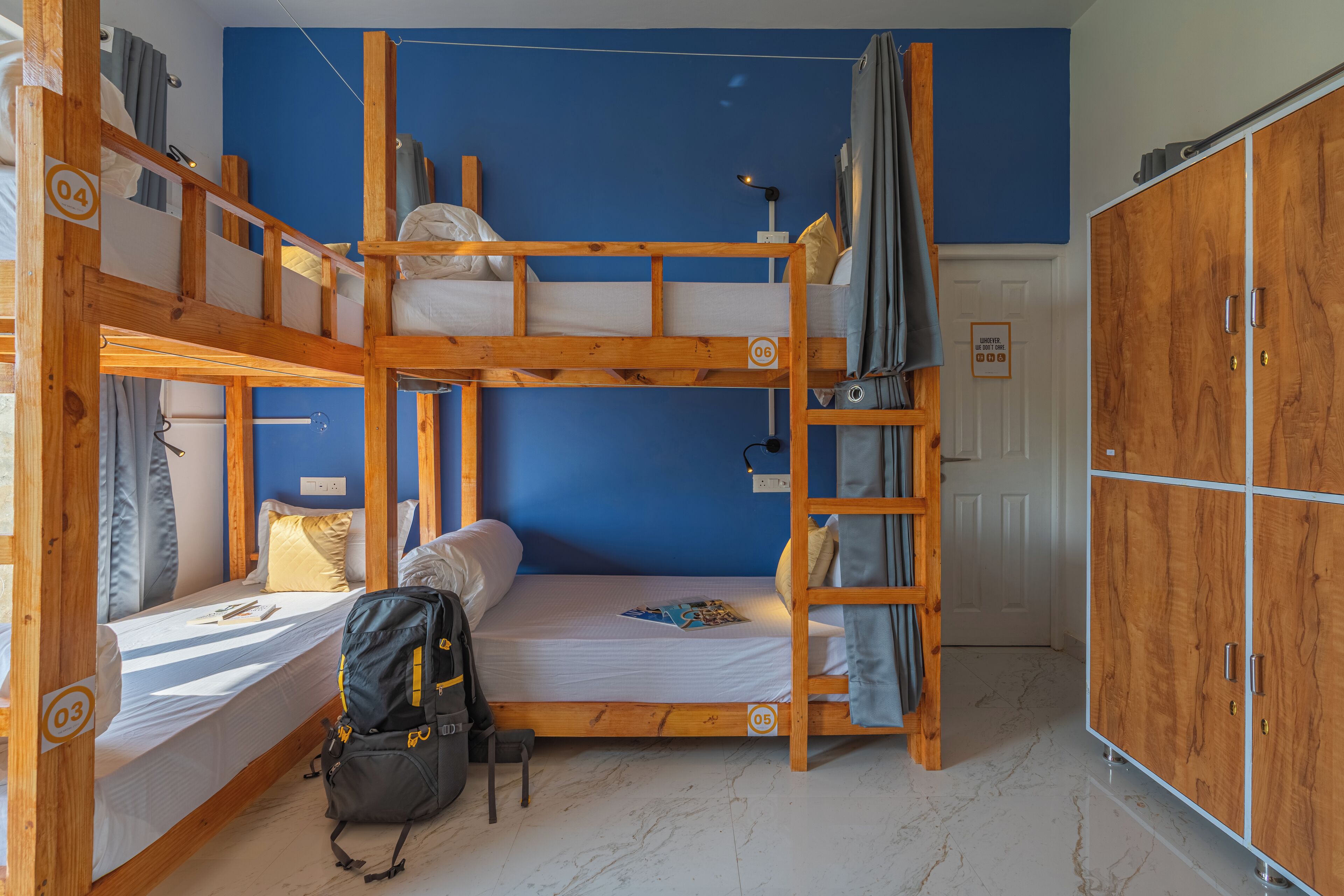 Camera con letto a castello, parete blu, mobili in legno, un'armadio e uno zaino sul pavimento.
