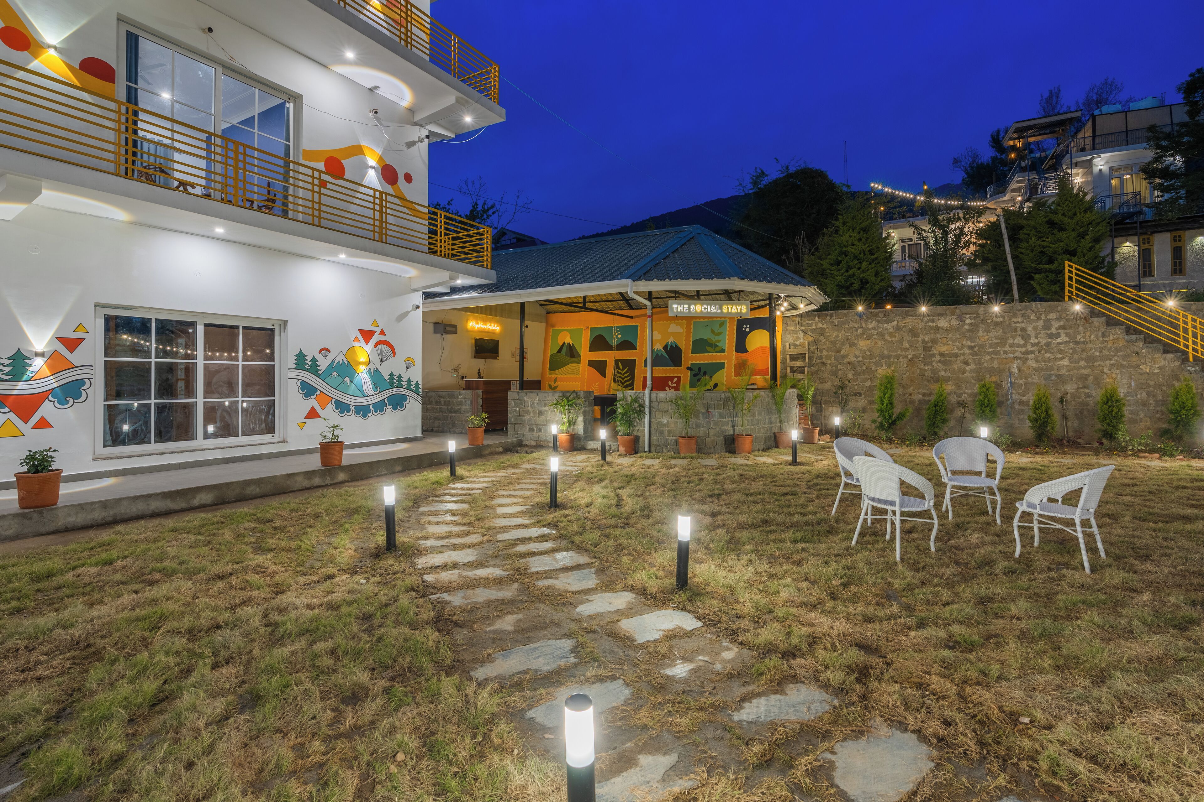 A modern building with a rooftop terrace, outdoor seating area, and a stone pathway leading to the entrance.