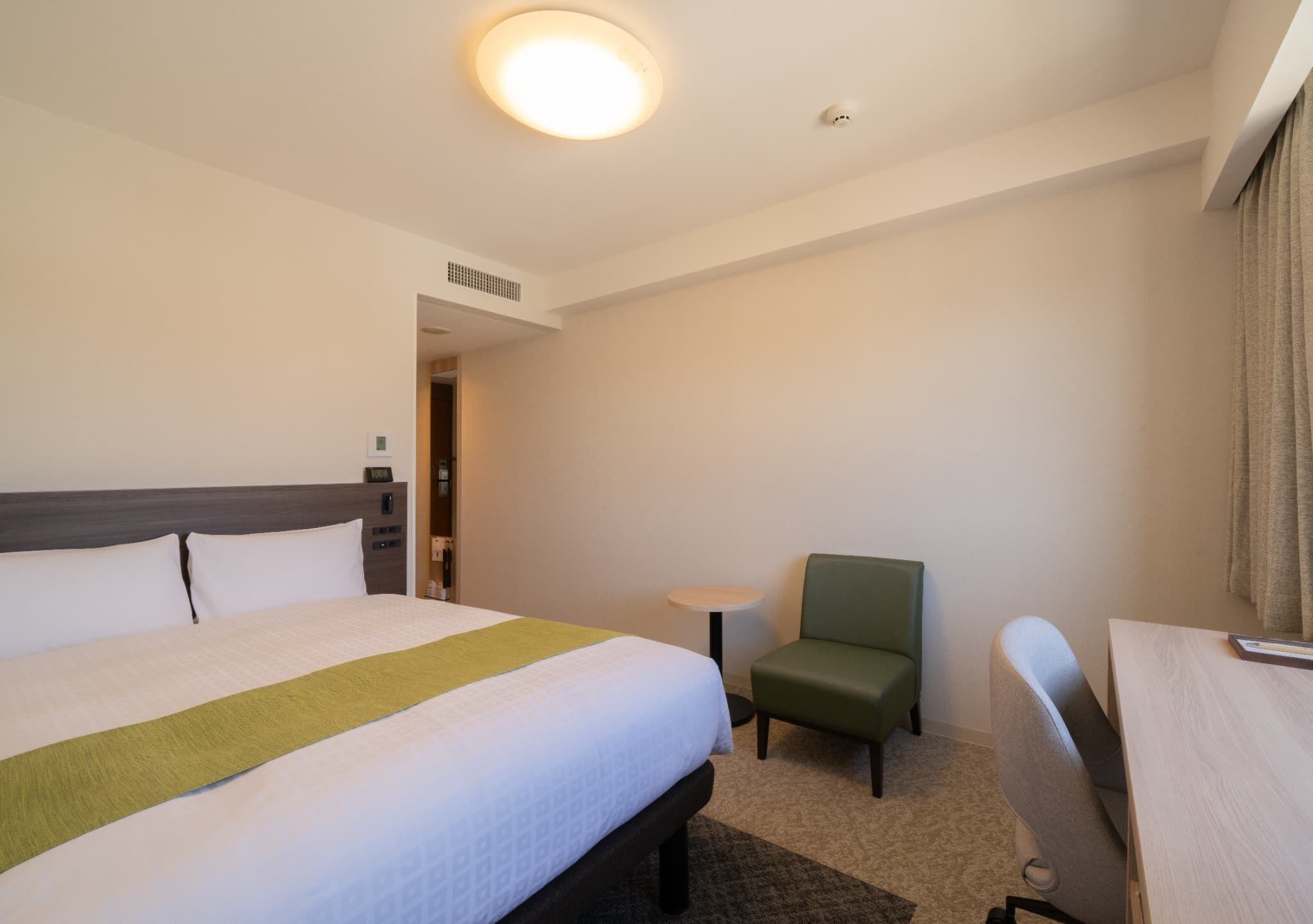 Una habitación de hotel con una cama grande, una mesita pequeña, una silla verde y un escritorio.