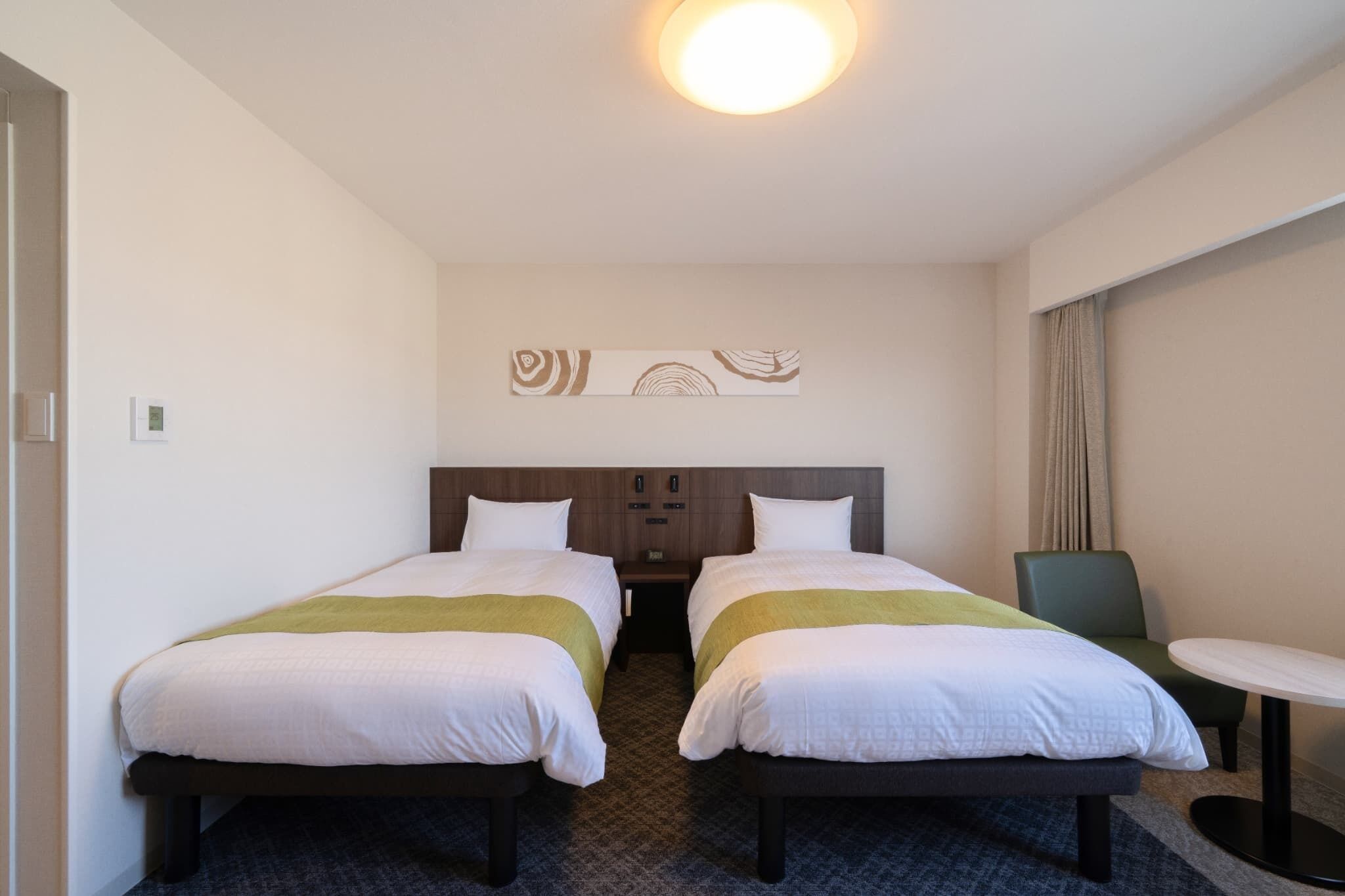 Une chambre d’hôtel avec deux lits, une petite table, une chaise et une œuvre d’art accrochée au mur.