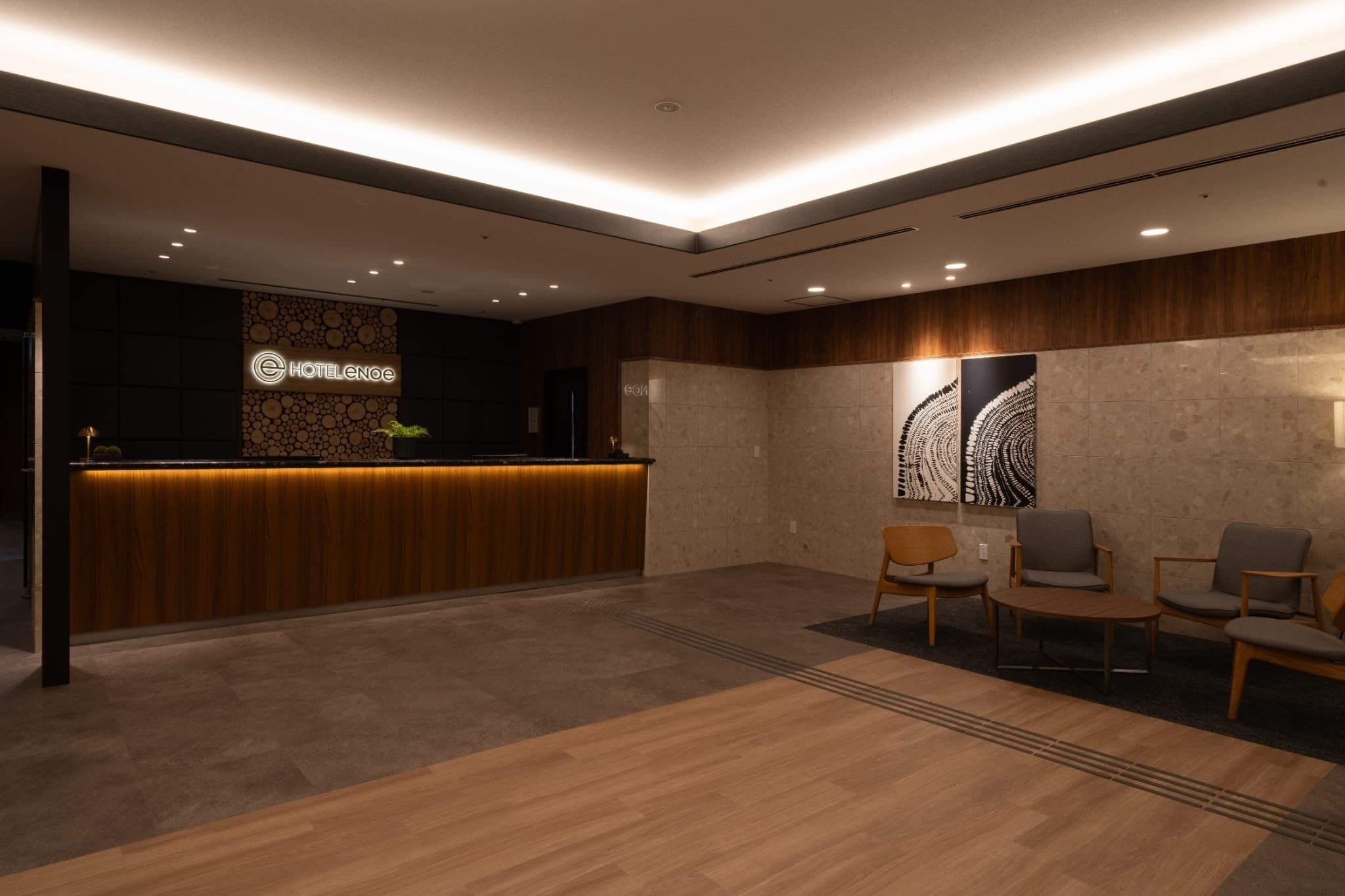 A hotel reception area with a wooden reception desk, a seating area with chairs, and a wall with a circular pattern and a large abstract artwork.