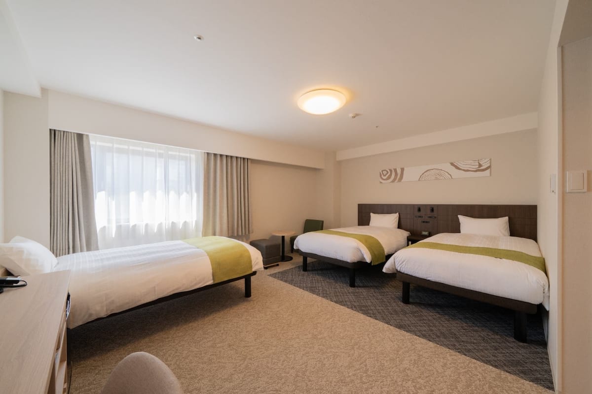 Habitación de hotel con dos camas, un escritorio, una silla, una mesita y una ventana con cortinas.