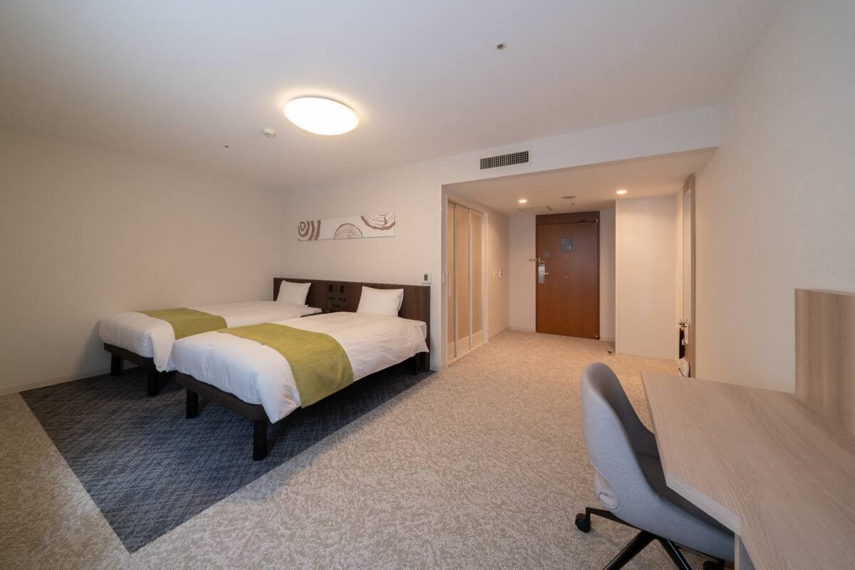 Habitación de hotel con dos camas, un escritorio y una puerta que da a otra habitación.