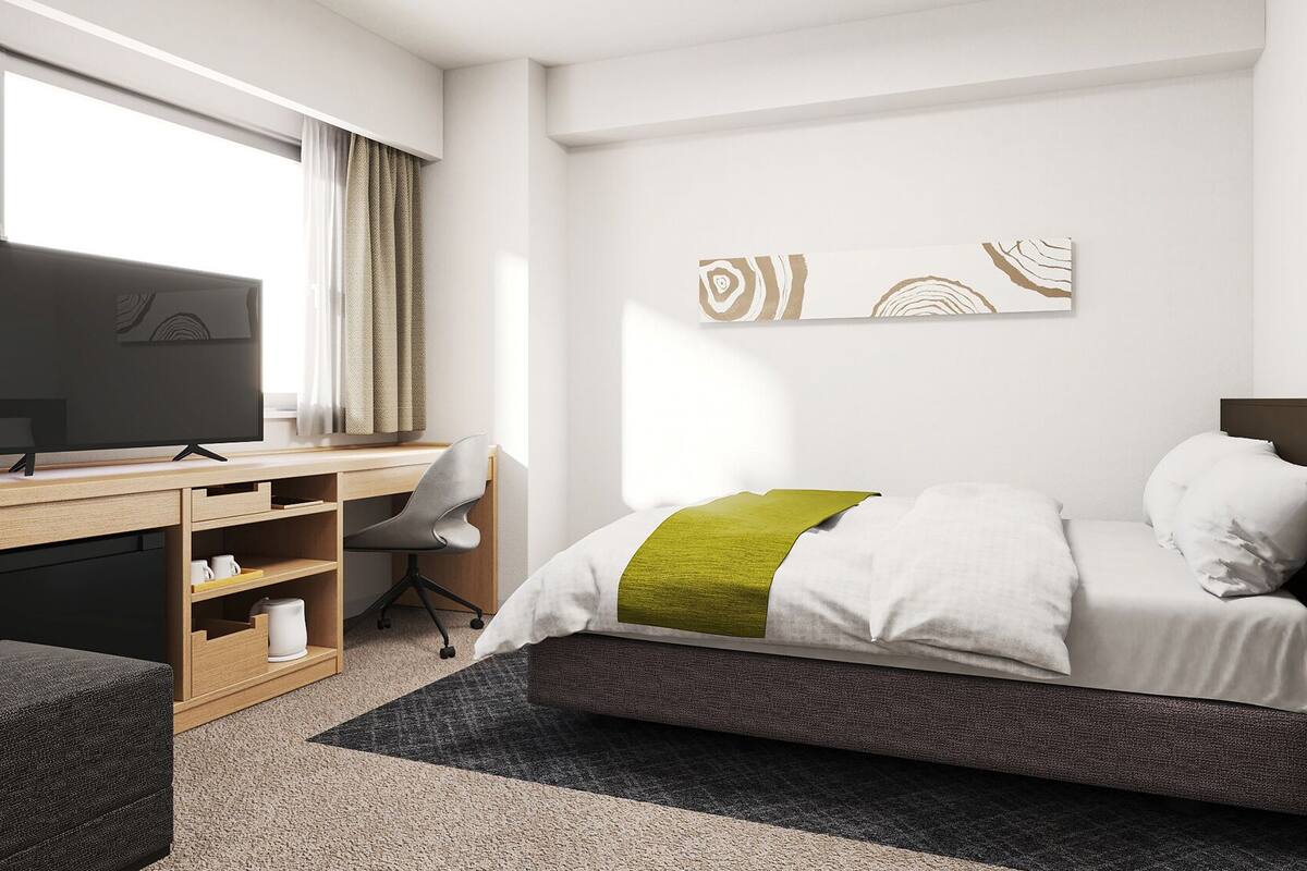 Una habitación de hotel pequeña con cama, escritorio, silla, televisor y armario.