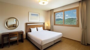Hotelkamer met een groot bed, een bureau, een stoel, een ronde spiegel, een inlijsting foto en een raam met uitzicht op de bergen.