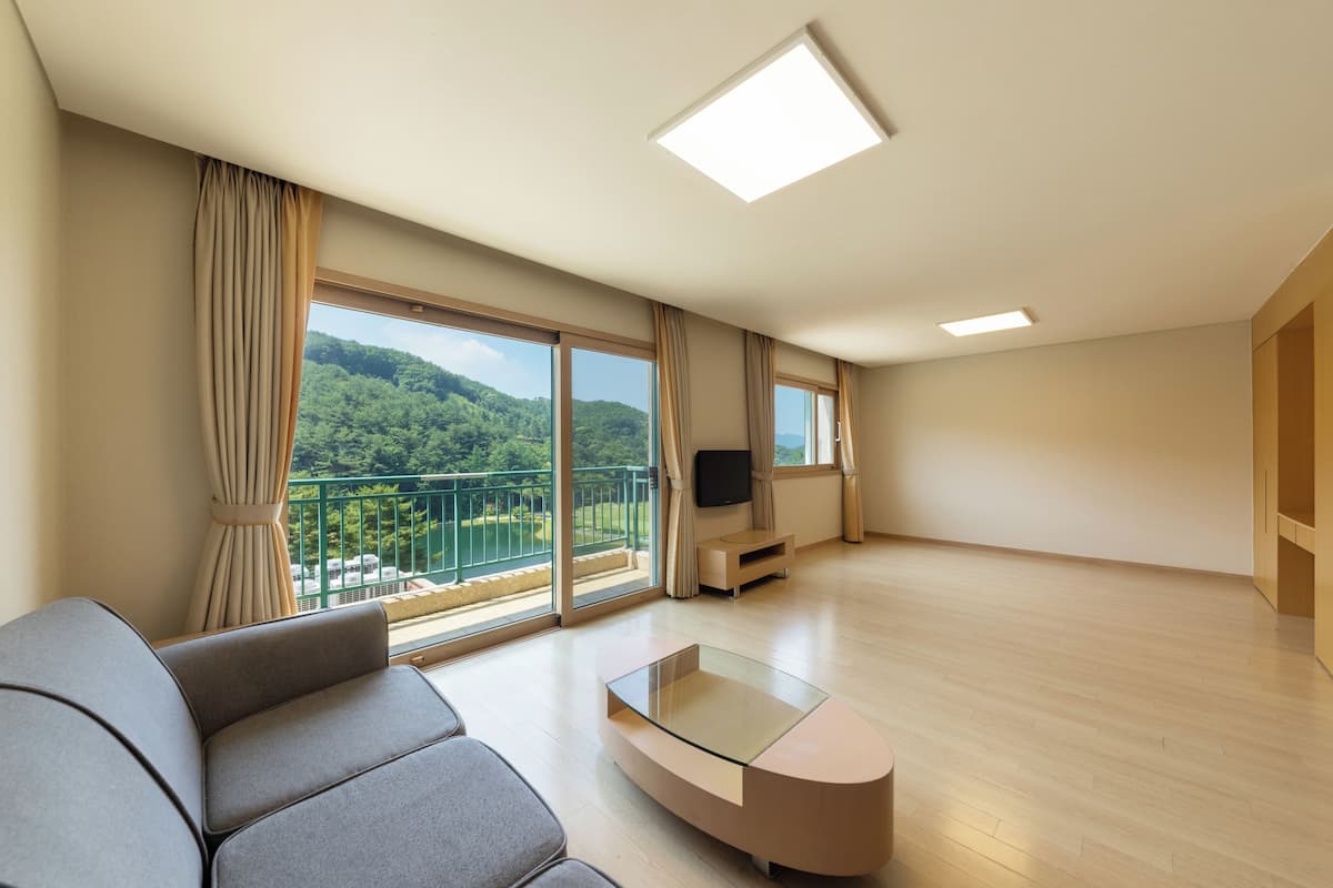 A modern living room with a large window, a sofa, a glass coffee table, and a flat-screen TV.