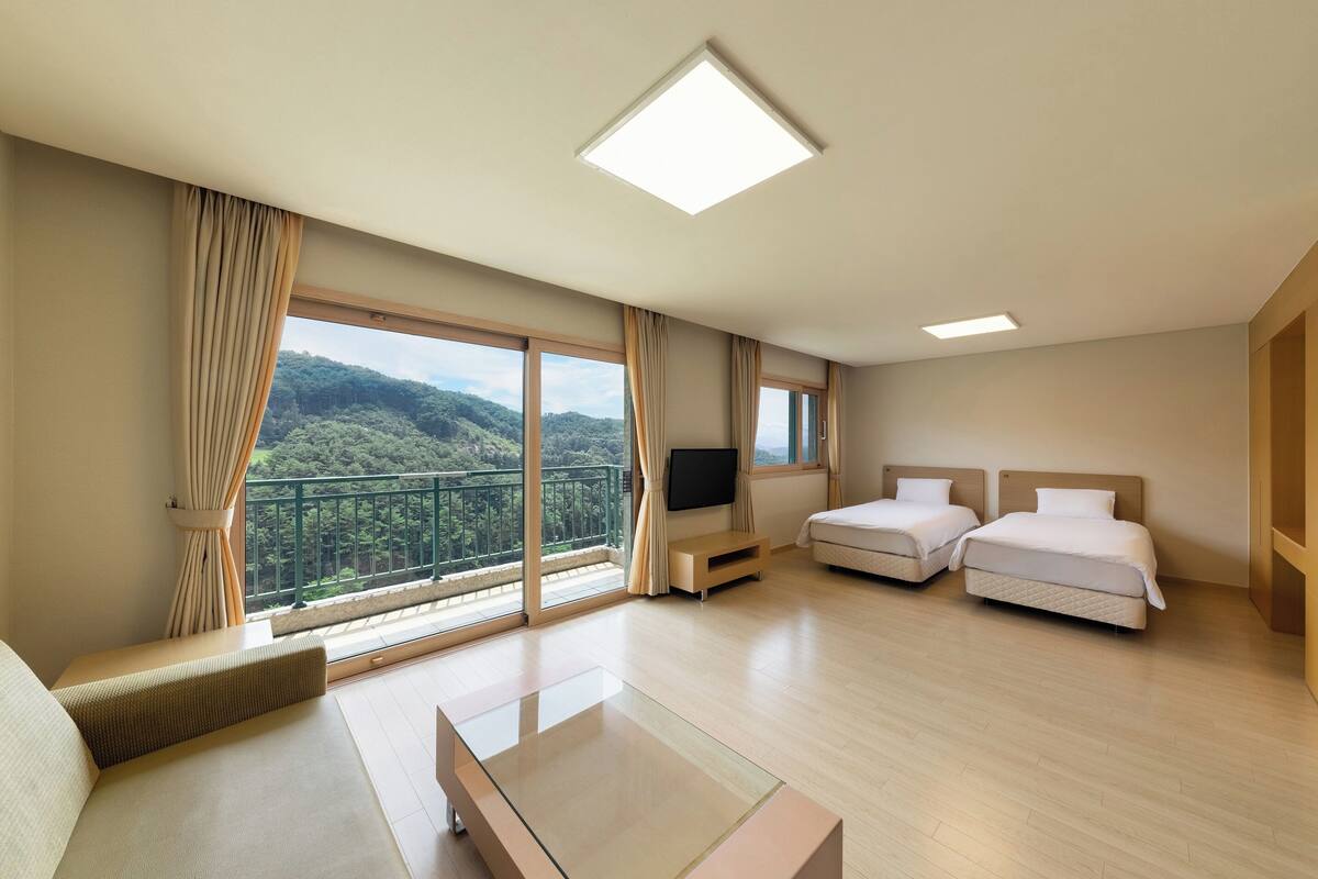 A hotel room with a balcony, two beds, a TV, and a sofa.