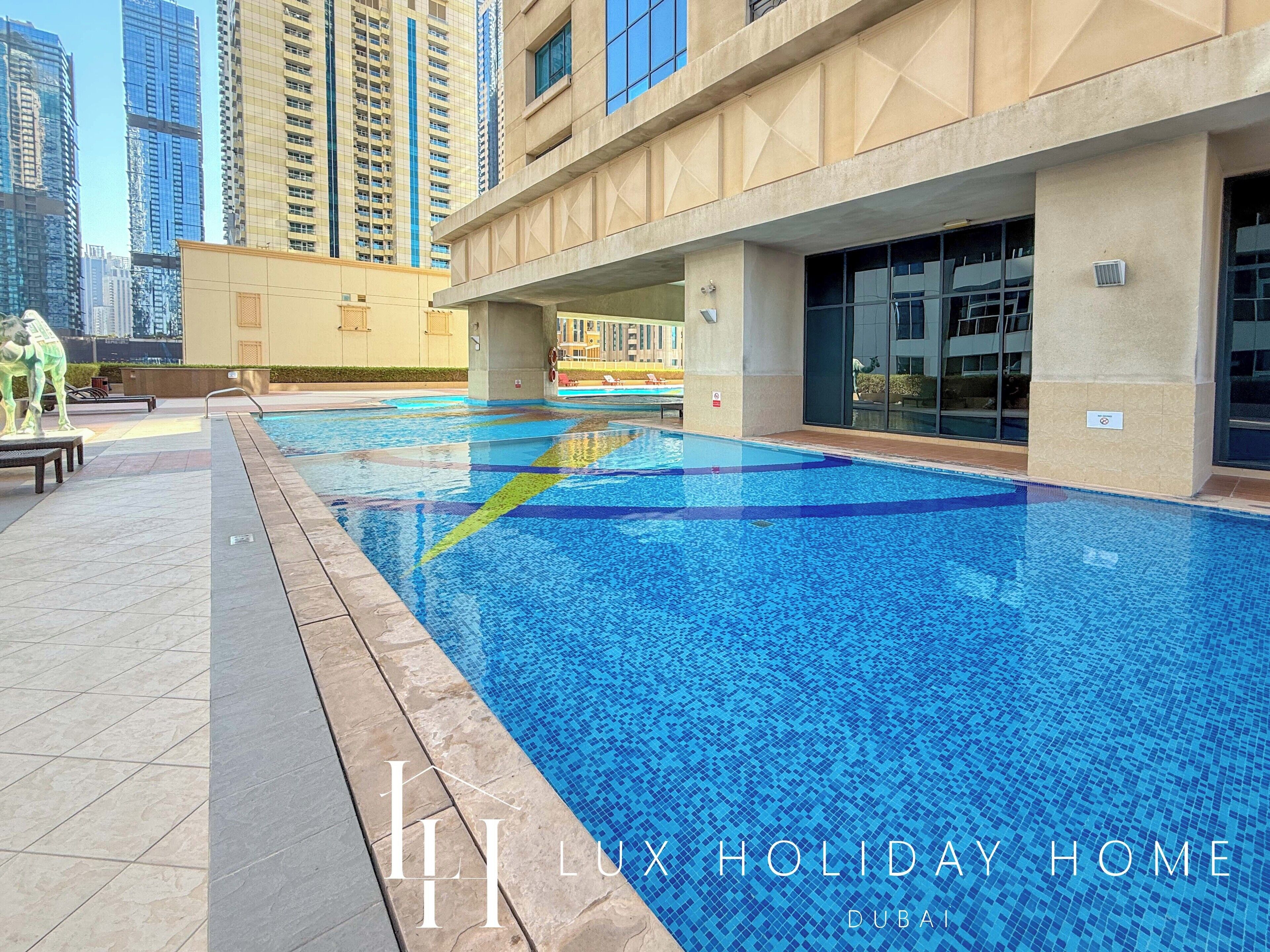 A swimming pool with a tiled edge, surrounded by a building with large windows and a beige facade.
