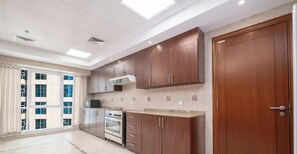 A spacious kitchen with wooden cabinets, a built-in oven, and a large window offering a view of the city. - LUX The Al Seef Marina Suite 2 (Dubai)