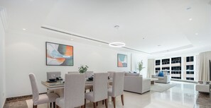 A modern, well-lit living area with a dining table and chairs, a sofa, and large windows offering a view. - LUX The Al Seef Marina Suite 2 (Dubai)