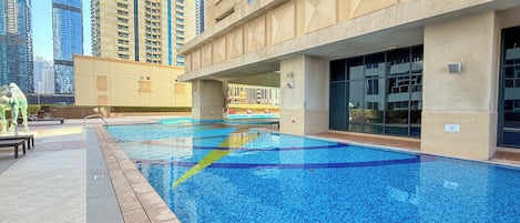 A swimming pool with a tiled edge, surrounded by a building with large windows and a beige facade.