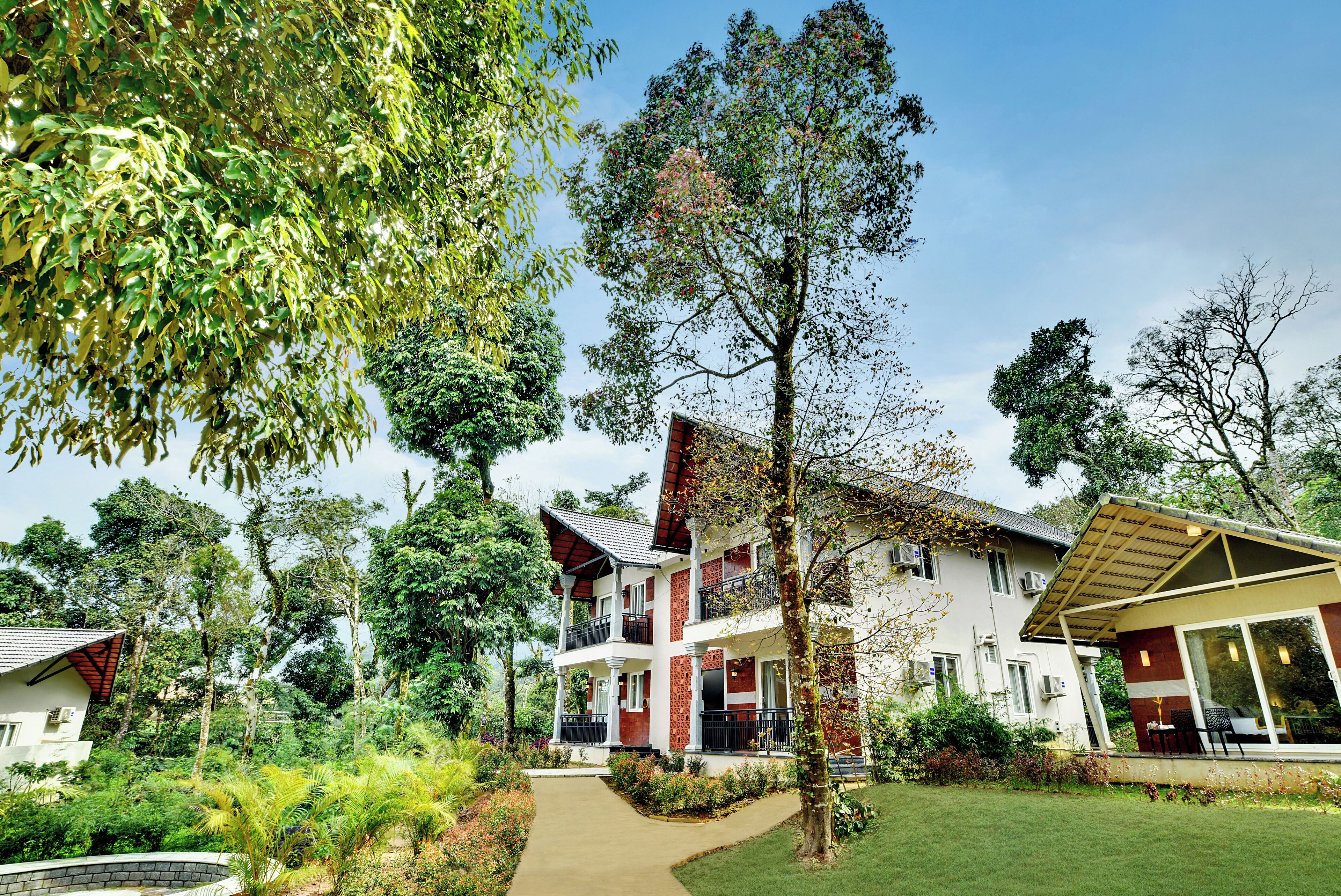 A two-story building with a balcony, surrounded by lush greenery and a clear sky.
