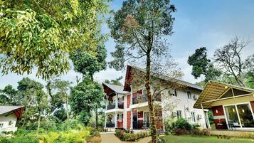 A two-story building with a balcony, surrounded by lush greenery and a clear sky.