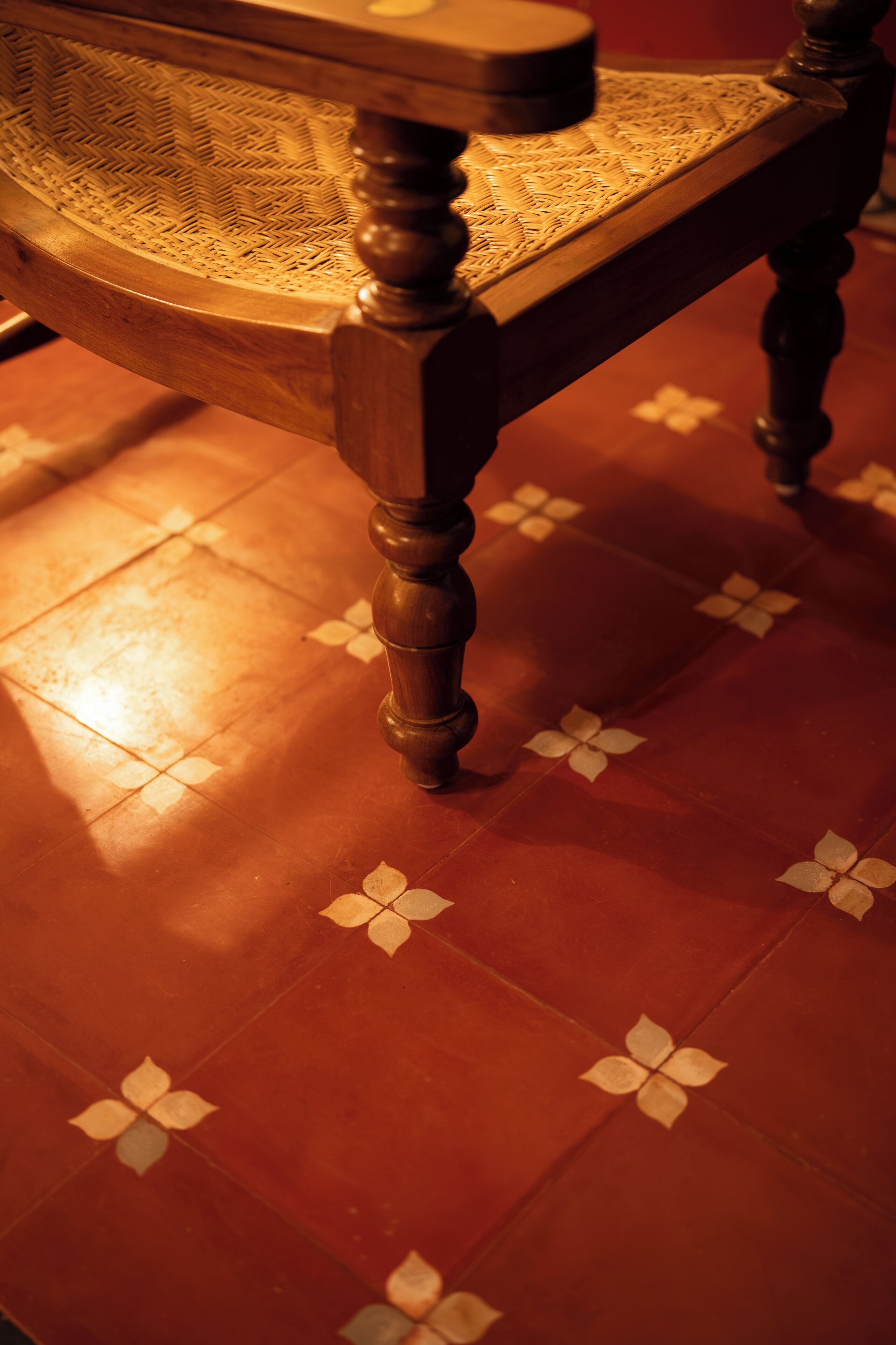 A wooden chair with turned legs and a woven seat, placed on a floor with a geometric pattern.