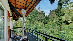 Ein Balkon mit Tisch und Stühlen, umgeben von üppiger Vegetation und Blick ins Waldgebiet.