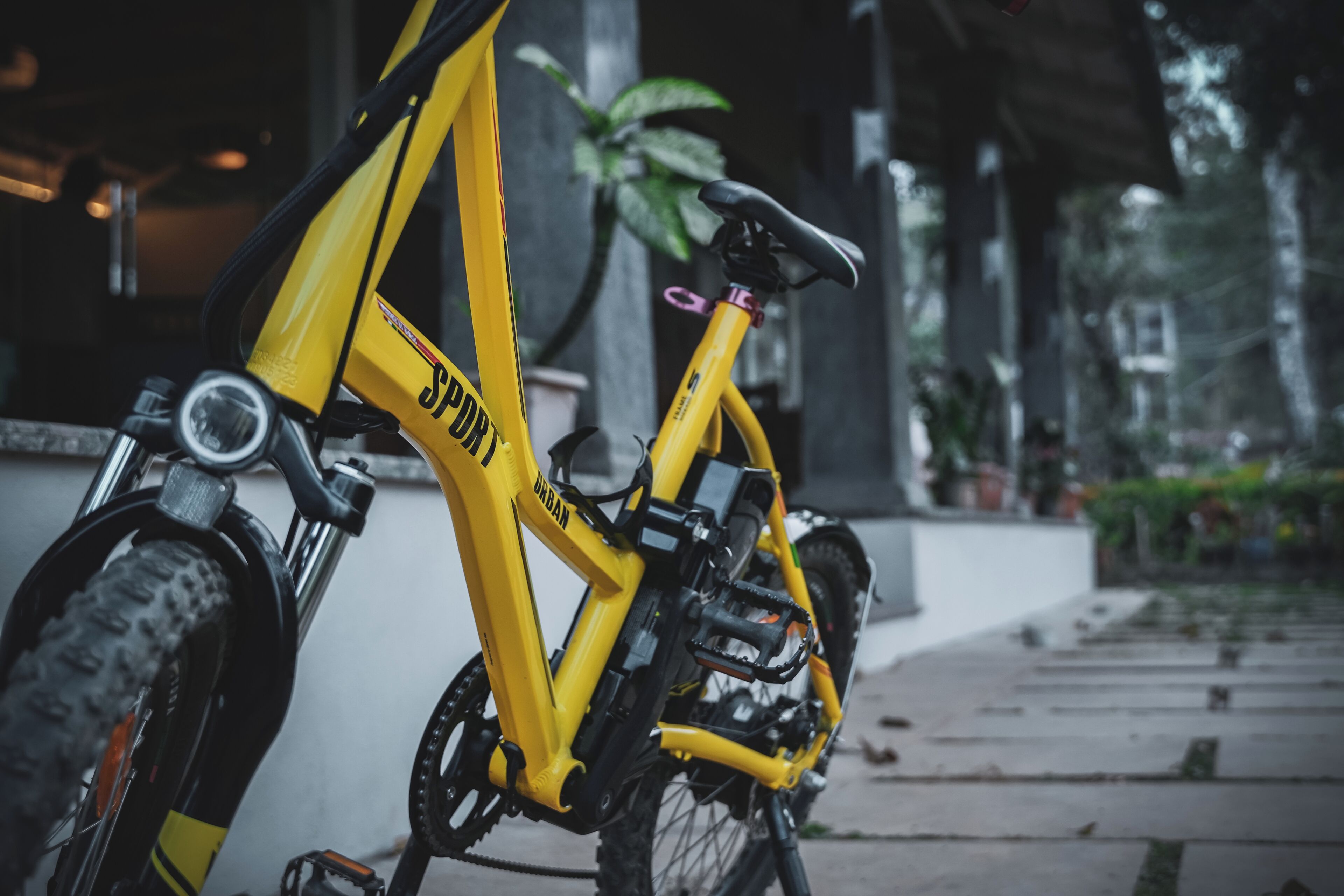 Una bicicleta amarilla con la marca "SPURT", estacionada en una acera con un edificio y plantas al fondo.