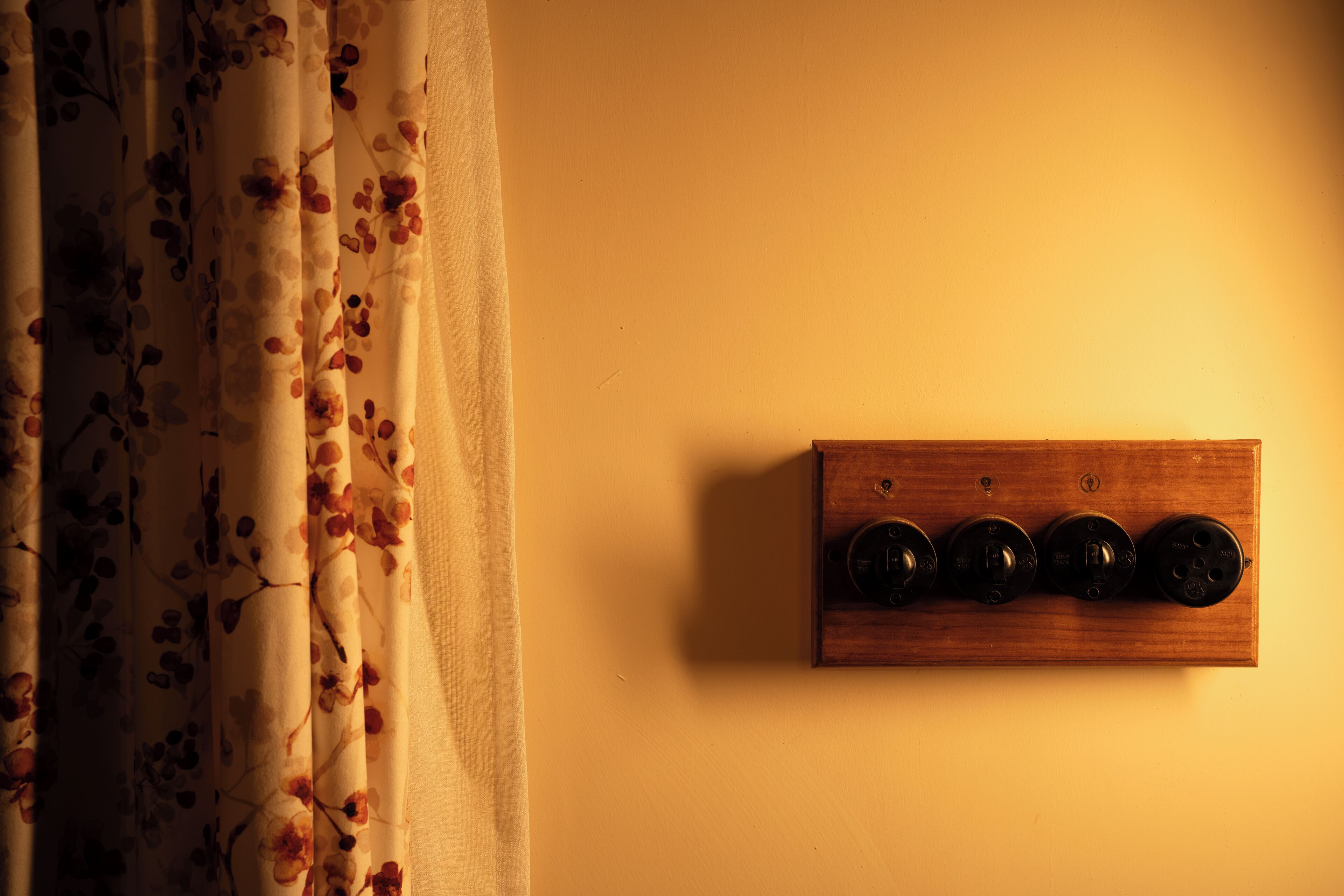 A wooden panel with four switches on a wall, next to a curtain with a floral pattern.