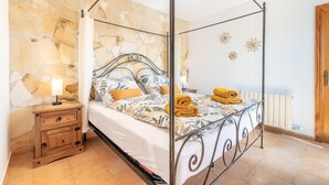 Una cama con dosel frente a una pared de piedra, una mesita de noche de madera con cajones y un radiador en la pared.