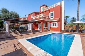 Un edificio de dos plantas con piscina, mobiliario exterior y una pérgola.