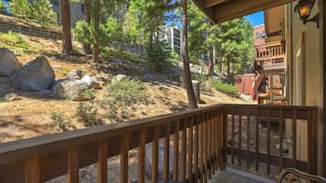 A wooden deck with a metal railing, overlooking a landscaped area with rocks and trees.