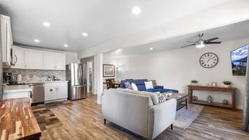 A modern living room with a sofa, a dining area, and a kitchen with white cabinets and stainless steel appliances.