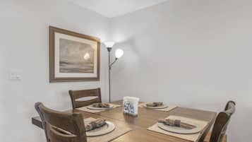 Een eethoek met een houten tafel, vier stoelen, een ingelijst schilderij aan de muur en een vloerlamp.