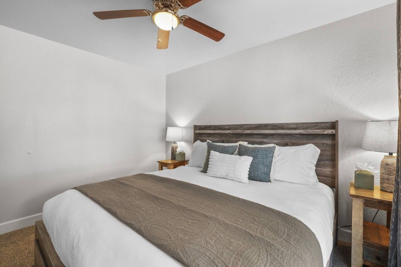 A bedroom with a bed, a nightstand, a lamp, a ceiling fan, and a wooden headboard.