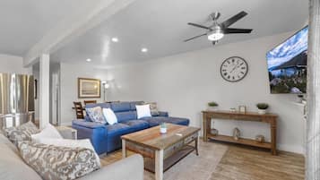 A living room with a blue sofa, a wooden coffee table, a clock, and a ceiling fan.
