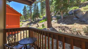 A wooden deck with a table and chairs, overlooking a forested area with rocks and trees.