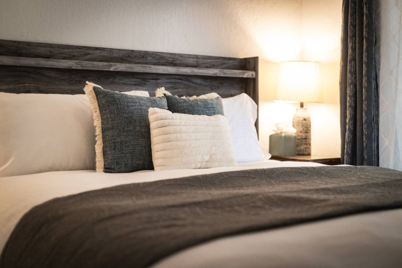 A neatly made bed with a dark headboard, white and grey pillows, and a grey throw blanket.