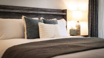 A neatly made bed with a dark headboard, white and grey pillows, and a grey throw blanket.