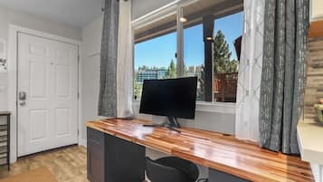 A compact kitchen with a wooden countertop, a black chair, a built-in dishwasher, and a window with curtains.