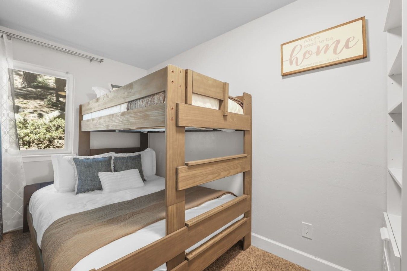 Een stapelbed met houten frame, wit beddengoed en een raam met uitzicht op groen.