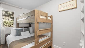 Een stapelbed met houten frame, wit beddengoed en een raam met uitzicht op groen.
