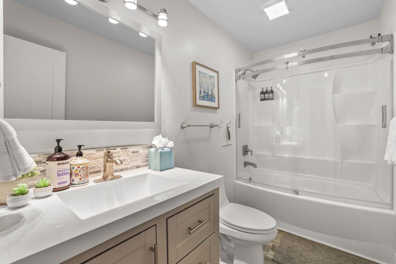A modern bathroom with a white vanity, a large mirror, a shower with a glass door, and a toilet.