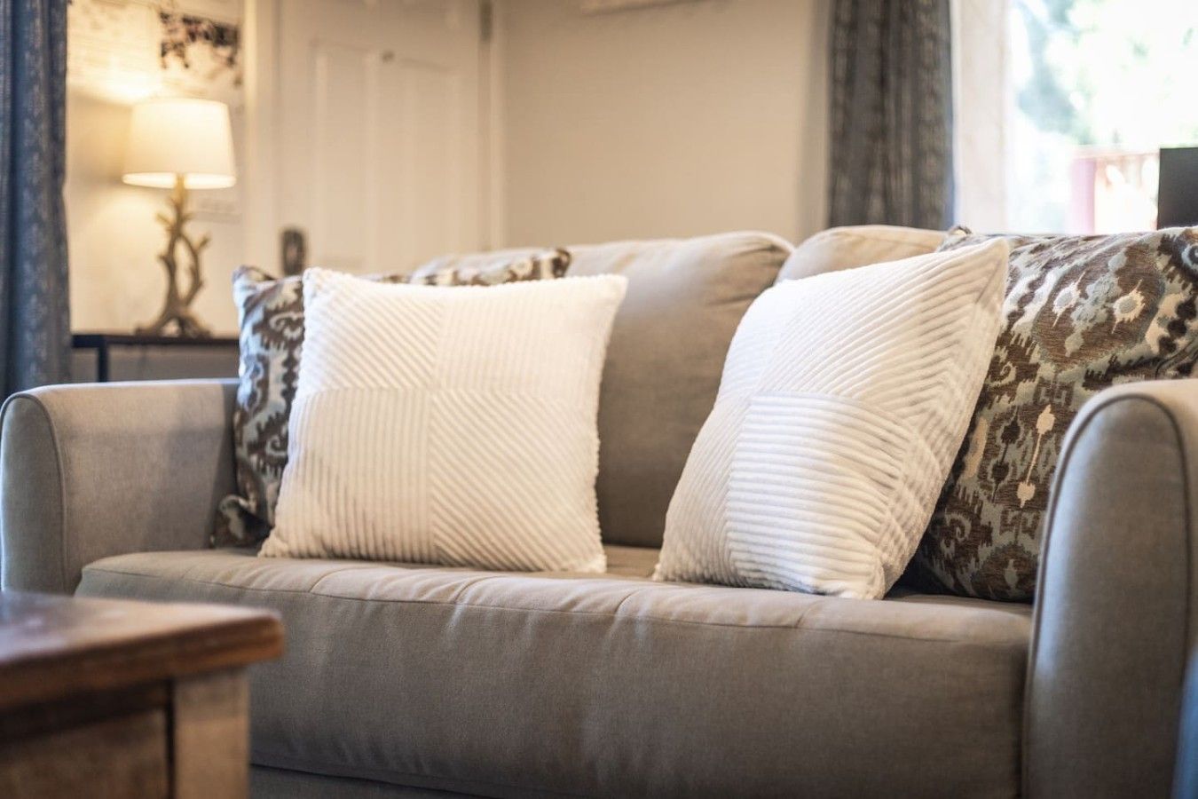 A grey sofa with two white pillows and one patterned pillow.
