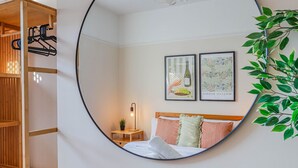A bedroom with a bed, a bedside table with a lamp, two framed pictures, a mirror, and a wooden wardrobe. - Georgia Suite | Stylish 1BR • Sleeps 4 • Wifi (Vale of Glamorgan)