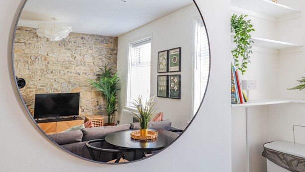 A modern living room with a stone wall, a round mirror, a sofa, a coffee table, and a TV. - Georgia Suite | Stylish 1BR • Sleeps 4 • Wifi (Vale of Glamorgan)