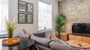 A modern living room with a stone wall, a large TV, and a cozy seating area. - Georgia Suite | Stylish 1BR • Sleeps 4 • Wifi (Vale of Glamorgan)