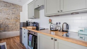 A compact kitchen with light grey cabinets, a wooden countertop, a stone wall, and a built-in oven. - Georgia Suite | Stylish 1BR • Sleeps 4 • Wifi (Vale of Glamorgan)