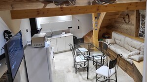 A compact kitchen with white cabinets, a dining table with chairs, and a sofa in a loft-style room with exposed wooden beams. - Cosy and comfortable 3* village house (Dorres)