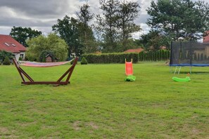 A grassy outdoor area with a hammock, a slide, and a swing set.