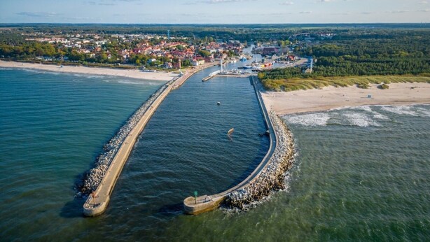 Eine Luftaufnahme einer Küstenstadt mit einer langen Pier, die sich ins Meer erstreckt, umgeben von Wohnhäusern und einem Sandstrand.