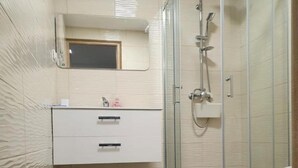 A bathroom with a glass shower enclosure, a white vanity with two drawers, and a mirror above the vanity.