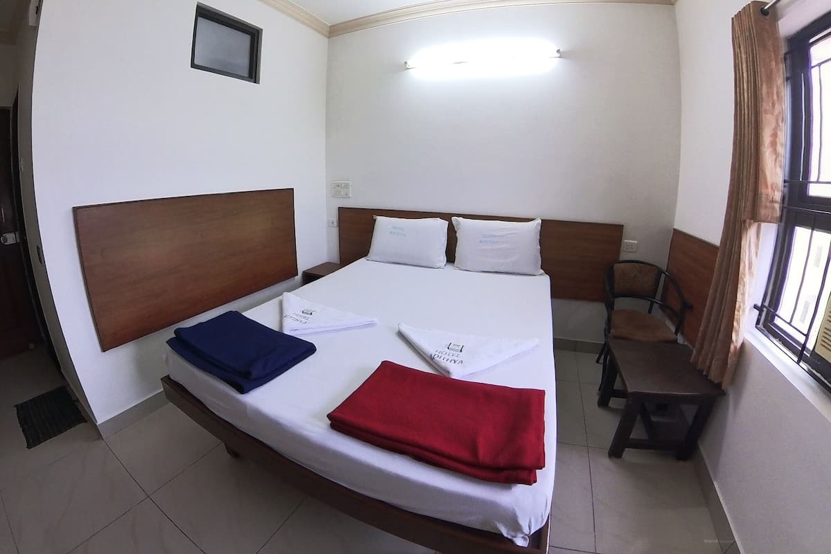 Habitación de hotel con cama, escritorio, silla, ventilador de techo y ventana con cortinas.