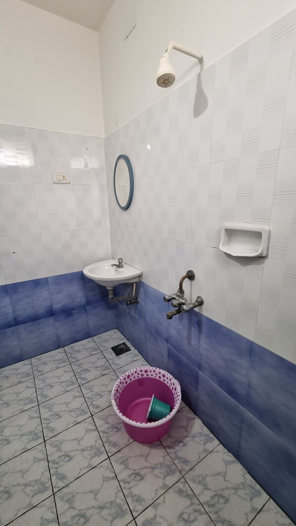 Une salle de bain avec un lavabo, un miroir, une douche et un seau posé sur le sol.