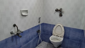 A bathroom with a toilet, shower, and a window. - Hotel adithya (Chennai)
