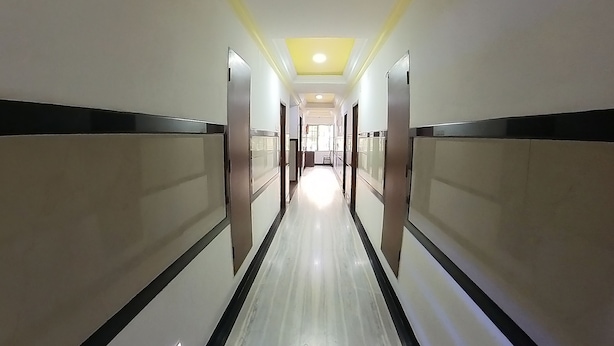 A long, narrow hallway with white walls and black trim, leading to a bright room at the end. - Hotel adithya (Chennai)
