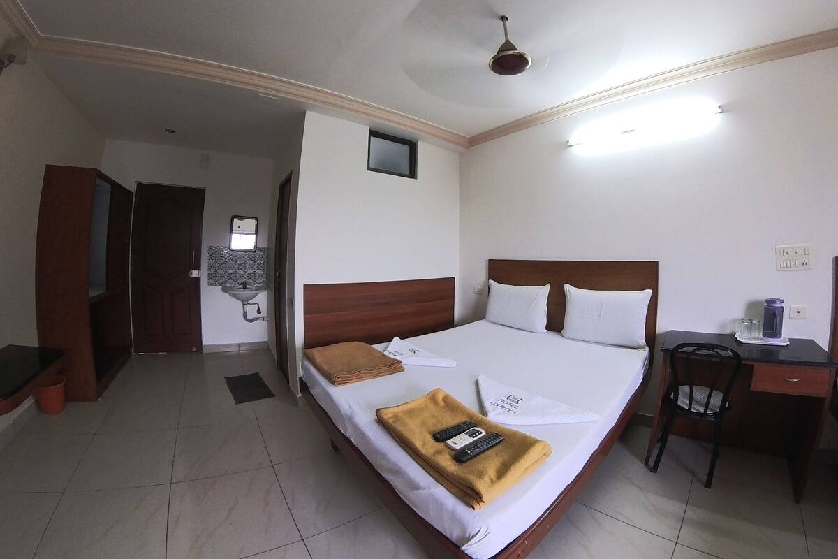 Habitación de hotel con cama, escritorio, silla, ventilador de techo, una ventana pequeña y lavamanos.